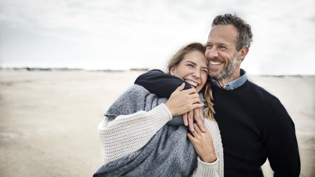 Un couple complice et souriant s’enlace sur une plage, symbolisant l’amour et la complicité après 20 ans de mariage, parfait pour illustrer les noces de porcelaine.